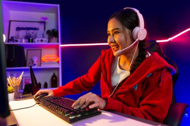 İnternet üzerinden kulaklık takıp gülümseyen Asyalı güzel kız flamasının sunucu kanalı izleyicilerle internet üzerinden konuşma yapıyor. Esport yetenekli takım oyuncuları neon mavi odada. Taktik.