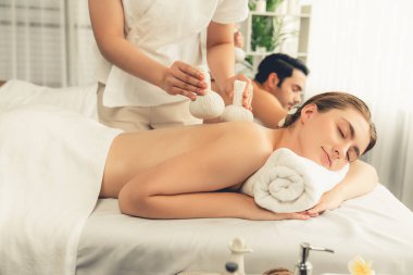 Sıcak bitkisel top spa masaj vücut tedavisi, masör nazikçe bitki torbasını çift müşteri vücuduna bastırıyor. Aromaterapi dinlenme sükuneti ve sükuneti kaplıca salonundaki atmosferi aydınlatıyor. Sessiz.