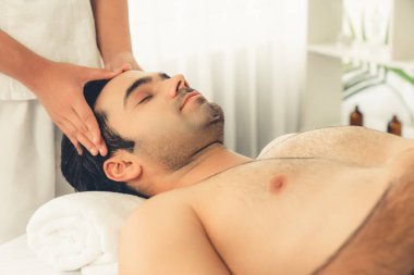 Beyaz adam stres önleyici kafa masajından ve lüks bir tatil beldesi veya otel spa salonundaki modern ışık ortamında yüz güzelliği eğlencelerini şımartmaktan hoşlanıyor. Sessiz.