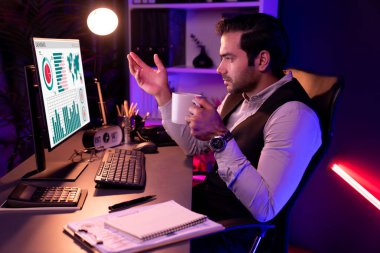 Gülümseyen zeki işadamı, elinde kahve fincanı olan satış ekibiyle buluşuyor ve geceleri Mor Neon Light Home Office 'deki bilgisayar ekranında ürün hedef pazarını araştırıyor. Tahmin et..