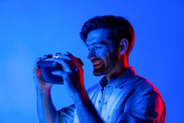 VR kulaklık takan ve metaevreni bağlayan adama yaklaş. Sanal gerçeklik kulaklığı takmaya hazırlanan bir adam ve neon ışıkta dururken sıradan bir gömlek. Teknoloji. Sapma.