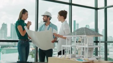 Profesyonel mimar mühendis ekibi konuşuyor, paylaşıyor, tasarım hakkında beyin fırtınası yapıyor. Yönetici planı dinlerken genç mimar plan yapıyor. İzleme