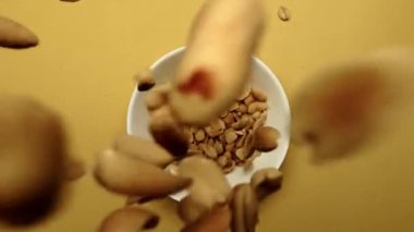 Fıstığın sarı arka planlı beyaz kaseye düşüşünün üst görüntüsü. Fıstığın makrografisi canlı sarı bir arka planda beyaz bir kaseye düşerken zarifçe görülüyor. Hava görüntüsü. Kapatın. Geliştirilebilir.