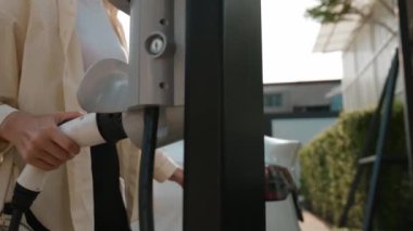 Ağır çekimde çalışan kadın şarj aletini şarj istasyonundan elektrikli araba aküsünü şarj etmek için kullandı. Sürdürülebilir çevre dostu seyahat konsepti için alternatif enerji ve şarj edilebilir EV araba. Yararlı