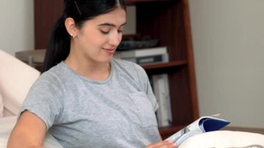 Kanepede oturan bir kadın ders kitabı okuyarak sosyal ve mesleki teknoloji bilgisini artırır ya da akıllı bir anne olmak için çocuk yetiştirir. Hayat boyu öğrenme konsepti. Uyumsuzluk.