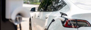Panorama afişi EV elektrikli araç ulusal parktaki ya da dışarıdaki EV şarj istasyonundan şarj oluyor. Çevre dostu EV arabalarla yaz ormanlarında doğal koruma. Yükselt