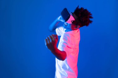 VR giyen Afro-Amerikan boksör boksör boksör, boksör yumruğu kamerasıyla fütüristik teknoloji sanal gerçeklik metaevren dövüş kutusunu birbirine bağlayan izole edilmiş pembe ışıklı duvar pozu veriyor. Entrika.