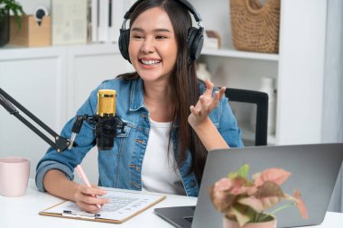 Sosyal medyada kulaklıkla canlı yayın yapan Asyalı sunucu modern stüdyoda yaşam koçluğu veya pazarlama dinleyicilerini selamlıyor. Taktik.