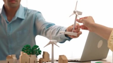 Temiz enerji ve ahşap blokla temsil edilen yel değirmeni modeli ekoloji evini sembolize ediyor. Yeşil enerji grafiği, dizüstü bilgisayarda çalışan iş adamının gelecekte ne yapacağına karar vermesi için dağıtıldı. Tanımlama.