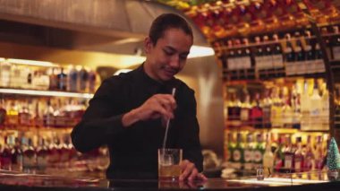 Zeki Asyalı barmen, bardakta karıştırılmış alkol şurubunu buzla karıştırıyor. Lüks gece kulübünde gece hayatı karışımı sergilenen özel bir içecek. Vinosity.