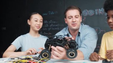 Akıllı öğretmen araba modelini farklı öğrencilere denetliyor. Melez ırk dinleyen liseli çocuklar masada dizüstü bilgisayarı ve kabloları olan robot model sistemini açıklıyor. Öğretim