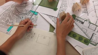 Mimar ve mühendis, mimari belge, ölçüm aracı ve ahşap bloğu ofis çevresinde dağıtan planlar kullanarak inşaat inşaatı hakkında düşünür veya tartışır. Tanımlama.