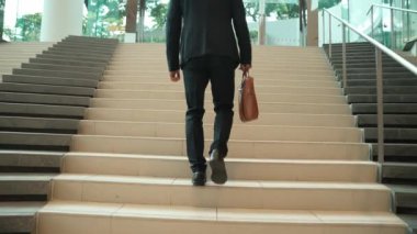 İş adamının bacağına yakın çekim merdivenleri çık. Başarılı bir adam merdivenleri çıkarken yeni bir şey keşfediyor. Seyahat etmek, terfi almak, yeni bir iş bulmak, yeteneğini artırmak. Arkadan bak. Sevinçli..
