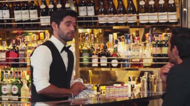 Güzel görünümlü barmen, VIP müşterisiyle içki tezgahında samimi, güler yüzlü bir şekilde sohbet ederken çekici bir profesyonellikle karşılama içkisi sunuyor ve harika bir ilk izlenim bırakıyor. Vinosity.