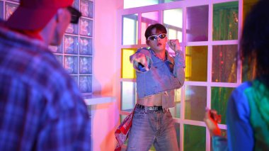 Ortasında dans eden profesyonel mutlu hipster onu alkışlayan çeşitli arkadaşlarıyla dans ediyor. Çekici Asyalı kırığı gece kulübünde neon ışığıyla enerjik adımlar atıyor. Mutluluk.