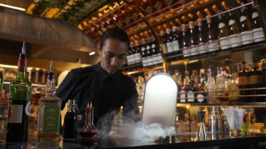 Asyalı barmen dumanlı klasik karışık viski kokteyli sunumu yapıyor. Harika bir sunum. İçecek tezgahı lüksünde özel, lezzetli, yaratıcı bir reklam içeceği öneriyor. Vinosity.