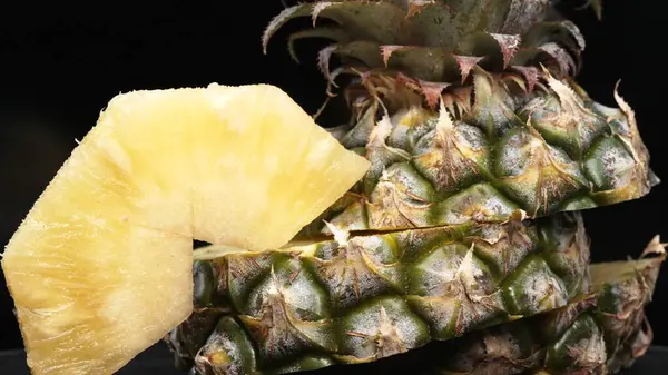 Taze ananaslı ve ayrı siyah arkaplanlı bir ananas dilimli videoyu kapat. Kaba ve balmumu kabuğu, dikenli yeşil yapraklardan bir taç, yemek fotoğrafçılığı. Geliştirilebilir.