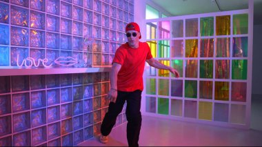 Komik break dansçı kameraya bakarken hiphop 'a doğru serbest adım atıyor. Çılgın mutlu hipster dans edip sokak dansı yaparken Led ışığında günlük kıyafet ve güneş gözlüğü takıyor. Mutluluk.