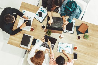 Modern ofisteki iş adamları ve iş kadınlarıyla grup toplantısındaki iş adamlarının en üst düzey görüşü, masada dizüstü bilgisayar, kahve ve belge ile. Kurumsal şirketler uds