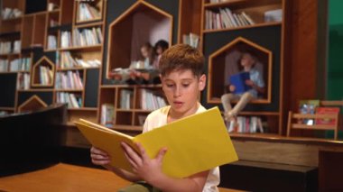 Bir grup zeki öğrenci kütüphanede otururken beyaz çocuk kitap okuyor. Çekici çocuk ders çalışıyor, çocuklar konuşurken romandan ya da kitaptan öğreniyor, eğitim hakkında sohbet ediyor. Etkinlik.