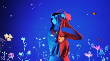 Güzel Asyalı kadın, VR ile metaevrensel etkileşimli sanal neon çiçekleri arasında kelebeklerle oynayan yeni neon çiçekleri mavi arka plan 3D grafik yüzen meta bahçe dünyası. Halüsinasyon.