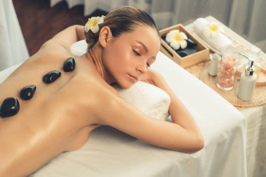 Lüks tatil köyündeki kaplıcalarda sıcak taş masajı. Gün ışığı sükunet ortamında, mutlu kadın müşteri bazalt taş masajından zevk alıyor. Rahatlatıcı bir sıcaklıkla vücudun üzerinde süzülüyor. Sessiz.