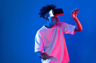 Sanal gerçeklik dünyasını dijital fütüristik teknolojiye bağlayan mavi pembe ışık duvarını gösteren 3 boyutlu hologram gösteren genç bir Afro-Amerikan oyun oyuncusu. Entrika.