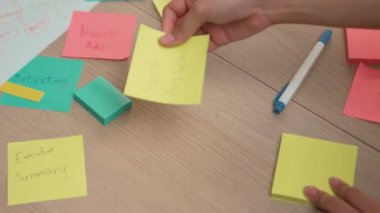 Yavaş çekimde, kadın iş kadını el yazısı pazarlama kâğıdı üzerine kalem ve yapışkan notlarla masaya yerleştirilmiş. Yaratıcı bir girişim ve takım çalışması konsepti. Eline odaklan. Değiştirilmiş.