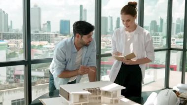 Beyaz mimar mühendis takımı ev modelini ölçmek için birlikte çalışıyor. Genç, güzel tasarımcı ev inşaatı yazarken erkek işçiler mimari modelleri inceliyor, inceliyor, inceliyor. Tartışma