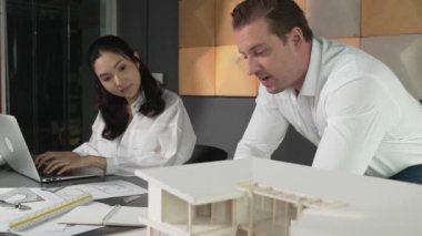 Ev planı çizmek için birlikte çalışan yetenekli mimar mühendisi. Mimar takımı, mimari model, plan ve dizüstü bilgisayarla ofis masasına yerleştirilen ev inşaatı hakkında tartışır. Yönlendirici.