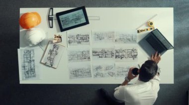 Proje planını kontrol ederken ve seçerken mimar mühendisin bina planlarını masaya yerleştirdiği tepeden aşağı hava görüntüsü. İç mimar toplantı masasından mimari plan seçti. Hizalama.