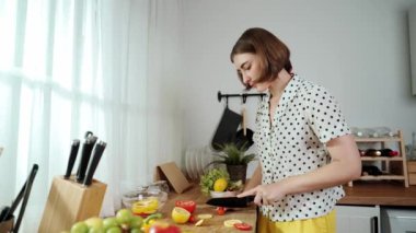 Enerjik anne, mutfak malzemeleri ile çevrili sebzeleri doğrarken modern mutfakta kahvaltı için salata yapıyor. Akıllı kadın temizlikçi yemek pişirir ve yemek hazırlar. Sağlıklı bir yaşam tarzı. Pedagoji.