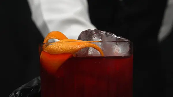 stock image Macrography, skilled hands of a bartender serving a Negroni cocktail, adorned with a vibrant fresh orange slice with black background. Each close-up shot captures the cocktail preparation. Comestible.