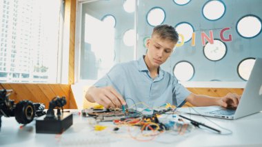 Akıllı mutlu çocuk araba modelini tamir etmek için elektronik alet kullanmayı öğreniyor ya da inceliyor. Lise öğrencisi STEM sınıfında otururken robotik makineleri tamir etmek için elektrikli aletler üzerinde çalışıyor. Öğretim.