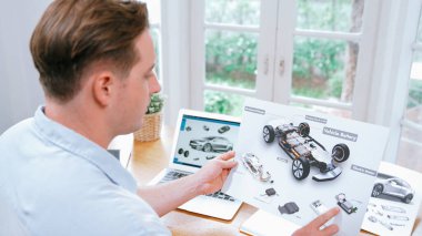 Araba tasarım mühendisi otomobil işi için otomobil prototipini ev ofisinde analiz ediyor. Otomotiv mühendisliği tasarımcısı dikkatle analiz ederek, dizüstü bilgisayarla araba tasarımında kusurlar ve iyileştirmeler buluyor.