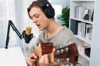 Gülümseyen yüzlü akıllı şarkıcının sunucu kanalı, şarkı söylerken gitar çalmak, sosyal medya kanalında yayın yapmak, modern stüdyo kaydında video kaydedici olarak kulaklık takmak. Bireysel.