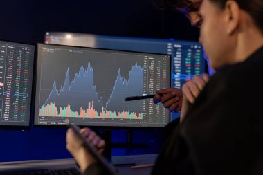 Bilgisayar ekranları üzerindeki dinamik borsa istatistiklerine el işaretleriyle odaklanmak, gece neon odasında risk yatırımını tartışan iki tüccarın tablet üzerindeki verilerini karşılaştırmak. Varsayım.