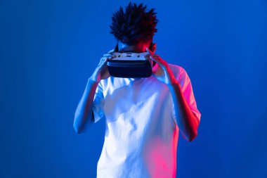 Sanal gerçekliği dijital fütüristik teknolojiye bağlayan pembe mavi neon duvarda VR 'dan bakan genç Afrikalı Amerikalı' ya şaşırdım. Entrika.