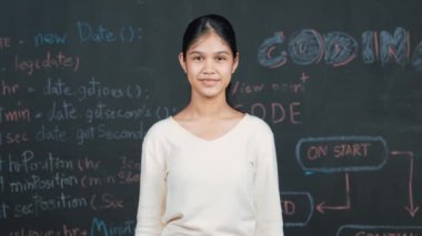 Genç öğrenci başarılı planını kutlarken kolunu kaldırdı. Mühendislik koduyla karatahtaya bakarken kameraya bakan mutlu genç, STEM sınıfında yazılı. Öğretim