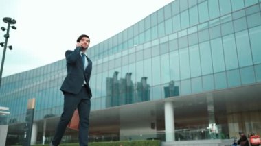 Akıllı iş adamı binada yürürken telefonla konuşuyor. İş planı, pazarlama stratejisi ya da çalışma hakkında konuşmak için akıllı telefonla konuşurken sokakta yürüyen mutlu bir yönetici. Sevinçli..