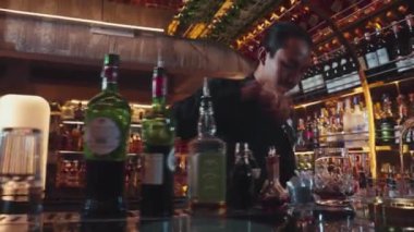 Asyalı barmen, kokteyl barında müşterilere ikram etmek için karıştırılmış bardağa buz küpü ve karışık kokteyl koyuyor. Hoş geldin içeceği ve etkileyici kostümlü profesyonellik ilk izlenimi. Vinosity.