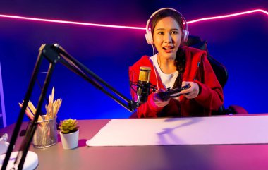 joystick 'li güzel Asyalı kız flamasının sunucu kanalı kulaklık takarak online oyun oynuyor Pastel renkli kulaklıklar takarak izleyicilerle çevrimiçi konuşuyor. Esport yetenekli takım oyuncuları neon odada. Taktik.