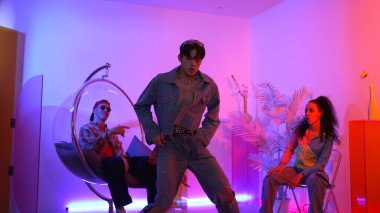 Çok kültürlü bir arkadaş kürsüde otururken Asyalı yetenekli bir dansçı modern müziğe geçiyor. Profesyonel dansçı, hipster takımı tezahürat yaparken ve desteklerken enerjik adımlar atıyor. Mutluluk.