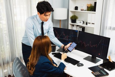 Gülümseyen işadamı cep telefonundaki dinamik borsa verilerini, iç ofisindeki internet sitesi uygulamasını analiz etmek için not yazan kadınlara gösteriyor. İnfobahn.