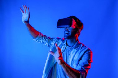 Heyecan verici bir sporcu el hareketi yaparken VR gözlüğü takıyor. Yetenekli genç ayakta duruyor ve teknolojik yenilikleri kullanarak gelecekteki sanal dünya programını veya metaevreni inceliyor. Sapma.