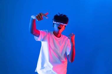 Genç Afrikalı Amerikalı oyuncu sanal gerçeklik dünyasını dijital fütüristik teknolojiye bağlayan mavi neon ışıklandırma duvarında sanal dünyada VR kullanarak bir hologramda yumruk kaldırıyor. Entrika.