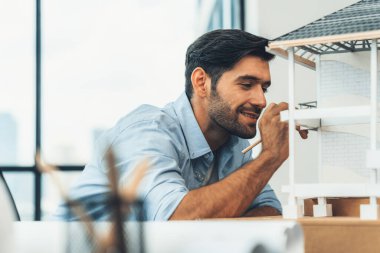 Akıllı beyaz mimar mühendisinin yakın plan portresi ev modelini incelerken aynı zamanda proje planı, proje planı ve ekipmanla birlikte mimar stüdyosunda inşaat yapmayı düşünüyor. İzleme.