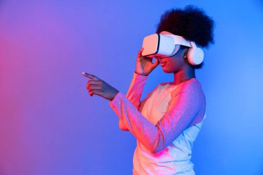 Genç Afrikalı, teknolojik dijital yenilik grafiğinde mavi neon aydınlatma grafiğinde izole edilmiş 3 boyutlu hologram veri uygulamasını seçmek için metaevren üzerinden VR gözlük takıyor. Entrika.