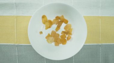 Sağlıklı sarı bir mısır gevreğinin bovlinge düşüşünü. Mısır gevreğinin beyaz ve siyah arka planda beyaz kaseye düşüşünün yukarıdan görünüşü. Makrografi. Ağır çekim. Kahvaltı konsepti. Pabulum.