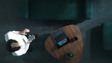 İş kadınının, proje yöneticisiyle telefonda konuşurken dizüstü bilgisayar ekranındaki mali grafiğe baktığı en tepeden aşağıya hava görüntüsü. Kadın odada dolaşırken yatırımcıya satışları bildiriyor. Müdürlük.